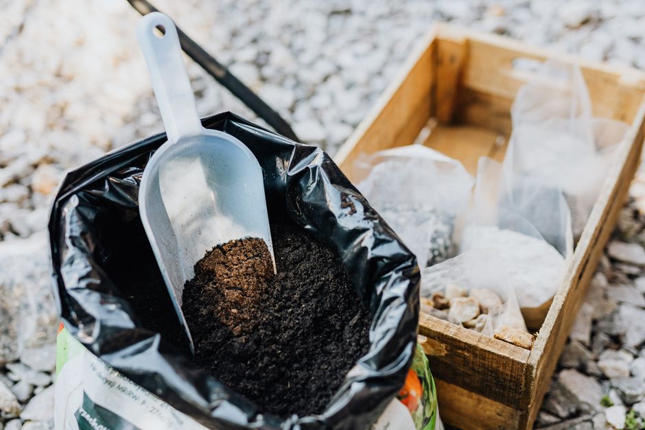 Open bag of dark garden soil with a scoop beside a wooden crate